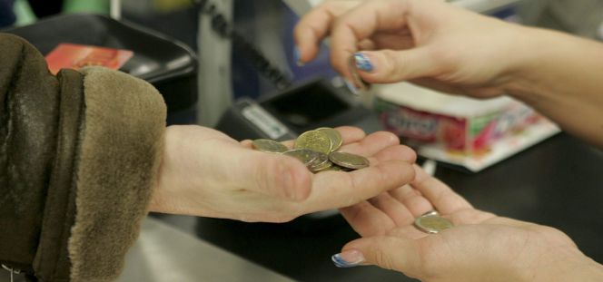 Una cajera ayuda a un cliente a contar las monedas de euro en un supermercado.