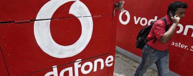 Un hombre habla con su móvil al lado de un logotipo de Vodafone.