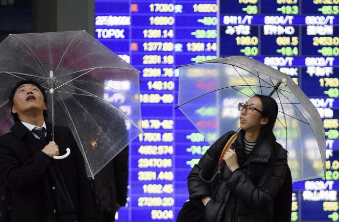 Un par de viandantes miran al cielo ante una pantalla que muestra información financiera en Tokio.