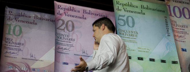 Un hombre habla por teléfono mientras camina frente a afiches de billetes venezolanos en la sede del Banco Centra de Venezuala (BCV).