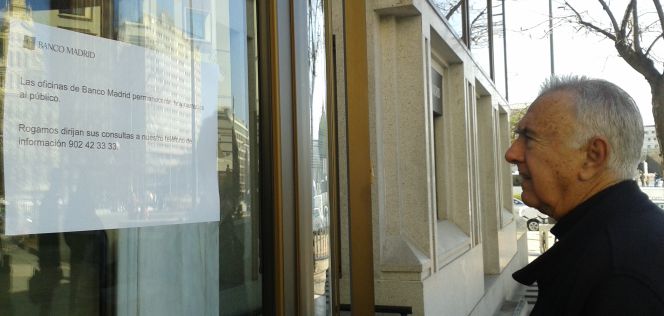Un viandante observa la comunicación en la que Banco Madrid informa del cierre de las oficinas, en su sede de la capital.