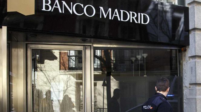 Un policía pasa frente a una oficina de Banco Madrid.