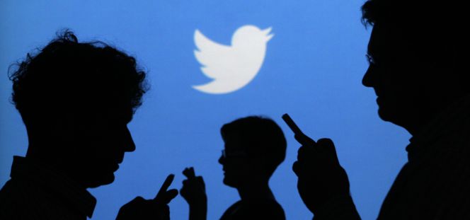 Varios usuarios utilizando un móvil con el logo de Twitter detrás.
