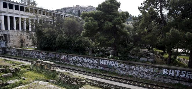 Dos jardineros en las ruinas del Agora romana con la Acrópolis al fondo.