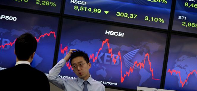Corredores de bolsa conversan junto a una pantalla que muestra información bursátil en Seúl (Corea del Sur).