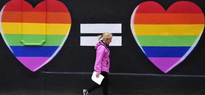 Una mujer camina junto a una pintada de dos corazones con los colores del arcoíris en Dublín.