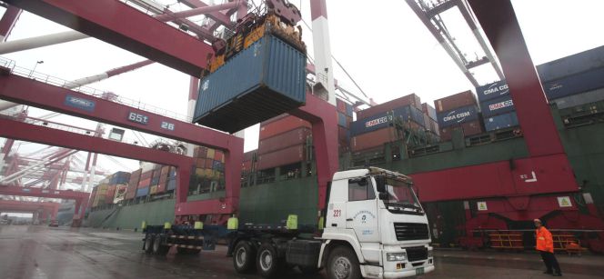 Un operario observa las labores de carga de un contenedor en un camión en un puerto.