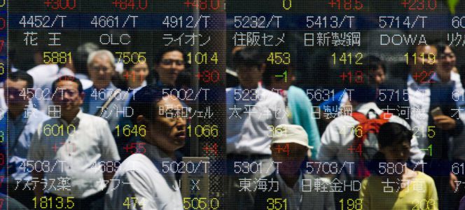Personas reflejadas en una pantalla con cotizaciones bursátiles, en Tokio (Japón).