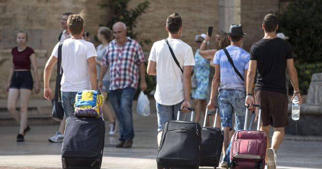 Cuatro jóvenes turistas caminan con su maletas en Valencia.