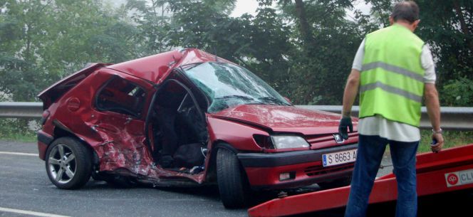 Un coche accidentado en una carretera de Asturias es recogido por una grúa.