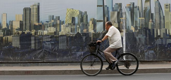 Un ciclista pasa junto a un cartel del diseño de un proyecto de construcción en Pekín.