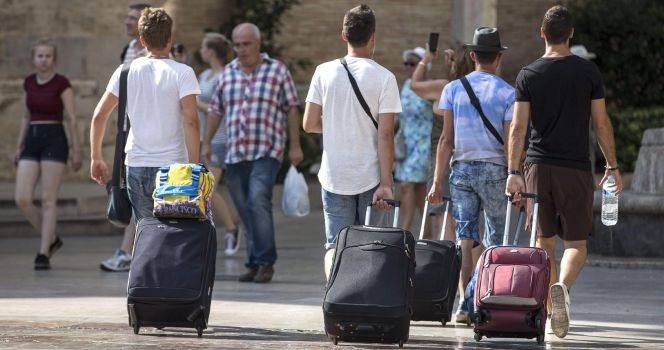 Cuatro jóvenes turistas caminan con su maletas por la plaza de la Virgen de Valencia.