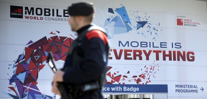 Un mosso d'esquadra ante la puerta de entrada de la Feria de Barcelona, que tiene ya todo a punto para recibir un nuevo Congreso Mundial de Móviles (MWC).
