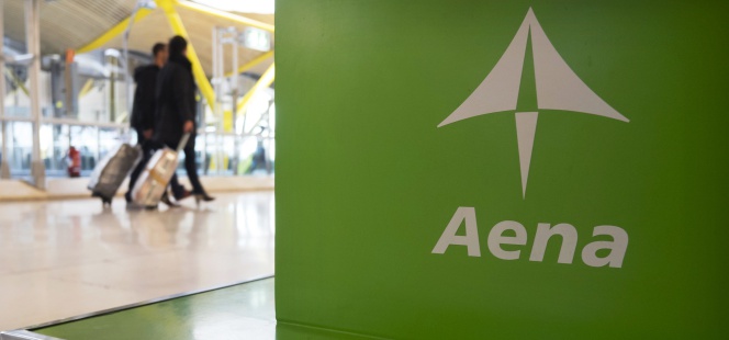 Dos viajeros pasan ante un 'stand' de Aena en el aeropuerto madrileño de Barajas.