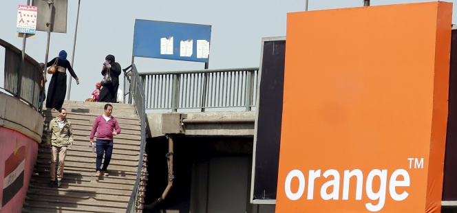 Varias personas pasean junto a un logo de Orange.