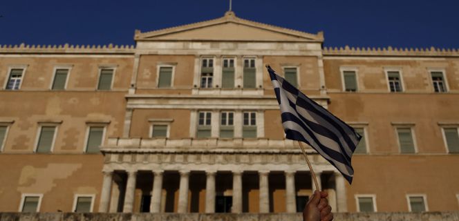 05072016. Un manifestante levanta una bandera de Grecia en una protesta antigobierno en el primer aniversario de las votaciones griegas para un referendo