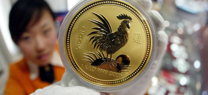 Una mujer muestra una moneda de oro con una imagen de un gallo, en Pekín.