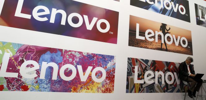 Un hombre utiliza un portátil junto a unos logos de Lenovo.