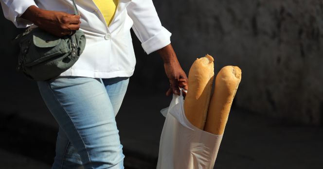 Una mujer camina con dos barras de pan en una bolsa de plástico.