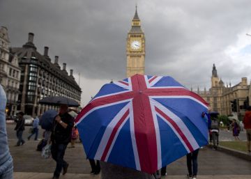 Una persona con un paraguas con la bandera de Reino Unido, delante del parlamento británico.