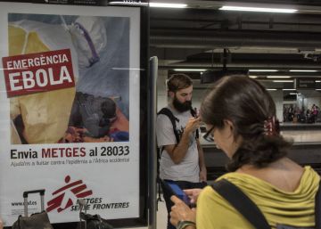 Unos turistas esperan un tren en la estación de Barcelona Sants junto a un cartel de lucha contra el ébola en 2014.