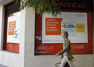 Un hombre pasando por delante de una oficina de Bankinter con una oferta hipotecaria