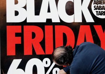 Un operario coloca un cartel en el escaprate de una tienda en la que anuncia grandes rebajas en el Black Friday.