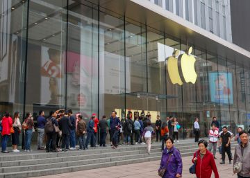 Una fila de clientes guarda turno frente a una tienda de Apple.