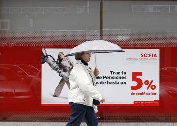 Una mujer pasa delante de una sucursal bancaria en la que se ofertan planes de pensiones.