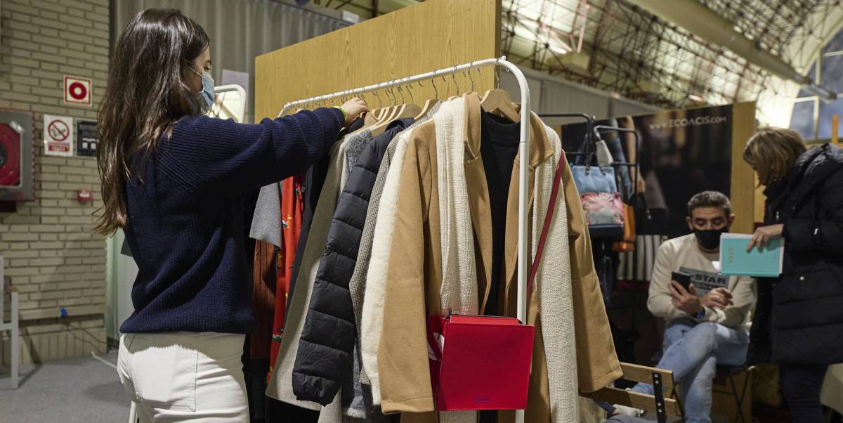 Una mujer ordena ropa en un puesto de comercio.