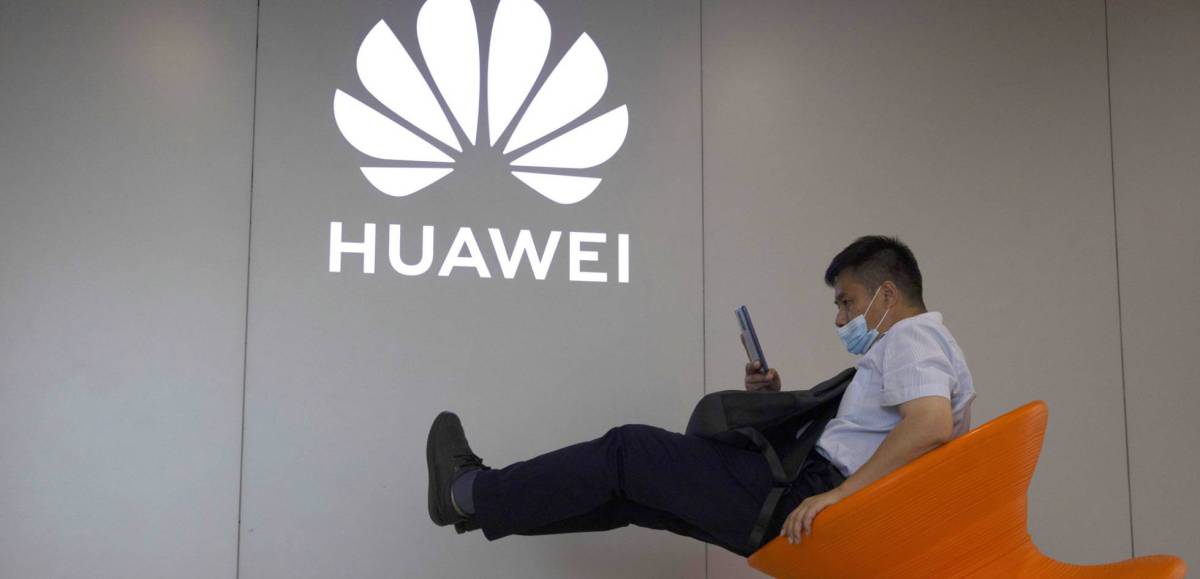 Un hombre consulta su móvil junto a un logo de Huawei.