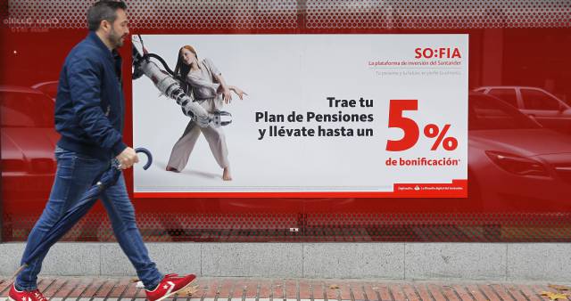 Una persona pasa delante de un cartel promocionando planes de pensiones, en una sucursal de Banco Santander.